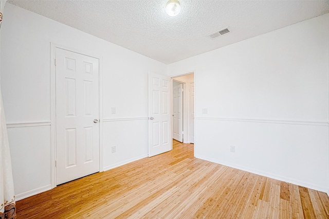 unfurnished bedroom featuring a textured ceiling, a closet, and light hardwood / wood-style flooring