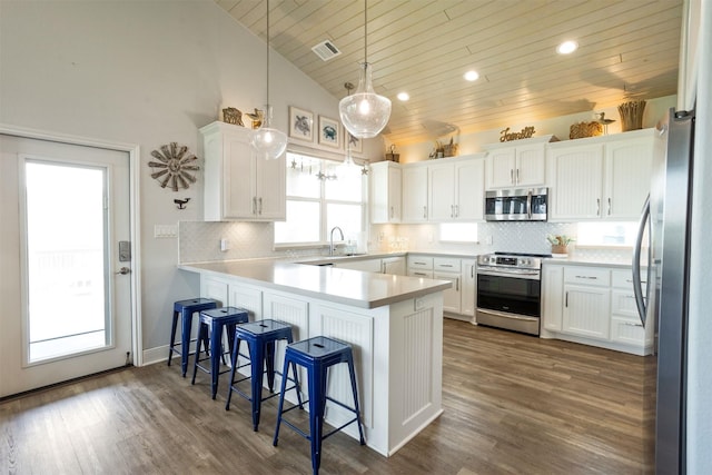 kitchen with kitchen peninsula, white cabinets, appliances with stainless steel finishes, and hanging light fixtures