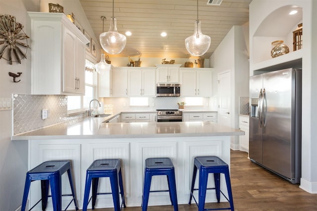 kitchen with pendant lighting, stainless steel appliances, a kitchen bar, backsplash, and white cabinetry