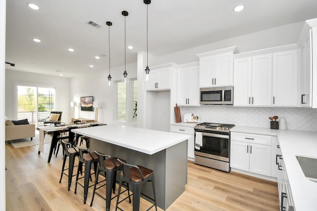 kitchen with a kitchen breakfast bar, stainless steel appliances, pendant lighting, white cabinetry, and backsplash