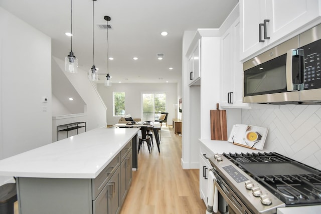 kitchen featuring gray cabinets, appliances with stainless steel finishes, white cabinetry, decorative light fixtures, and backsplash