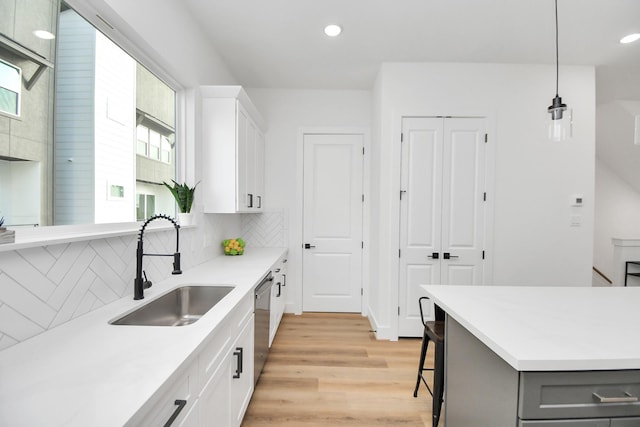 kitchen with decorative backsplash, white cabinets, decorative light fixtures, stainless steel dishwasher, and sink