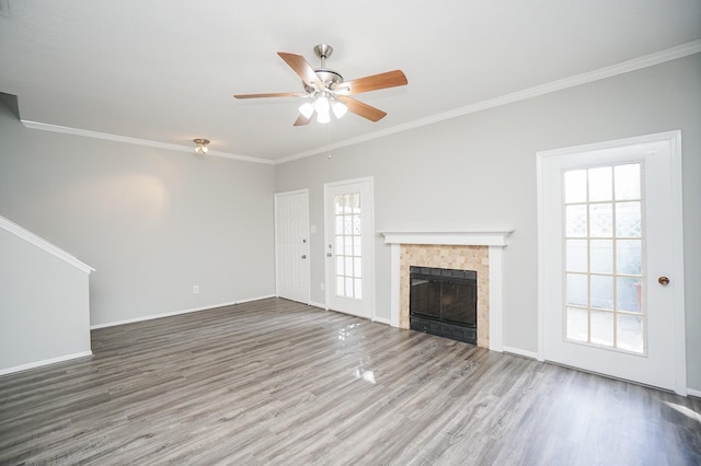 unfurnished living room featuring a tiled fireplace, crown molding, a wealth of natural light, and hardwood / wood-style flooring