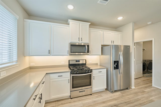 kitchen featuring stainless steel appliances, separate washer and dryer, light hardwood / wood-style flooring, and white cabinetry