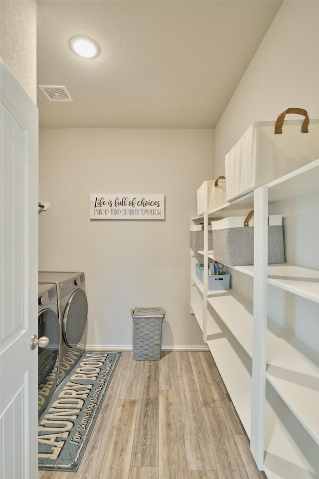 washroom with light hardwood / wood-style floors, a textured ceiling, and separate washer and dryer