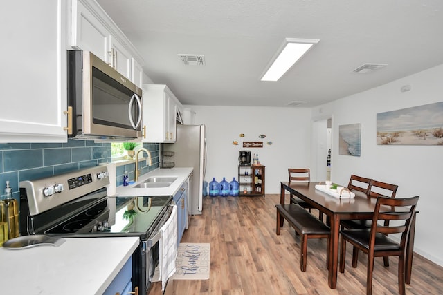 kitchen featuring sink, white cabinets, light wood-type flooring, backsplash, and appliances with stainless steel finishes