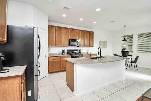 kitchen featuring light stone counters, light tile patterned flooring, pendant lighting, black appliances, and a kitchen island with sink