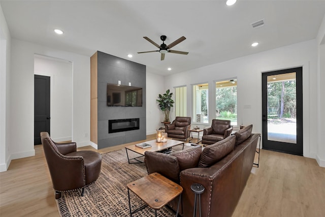 living room featuring a tiled fireplace, ceiling fan, and light hardwood / wood-style flooring