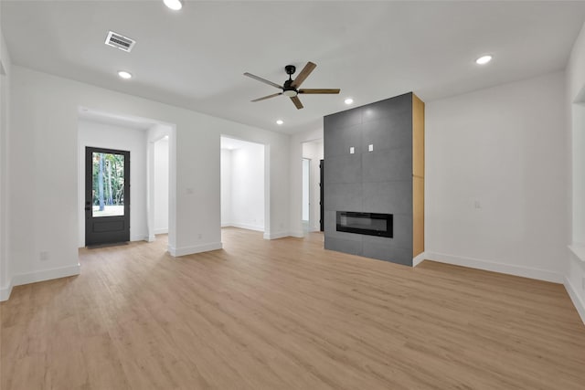 unfurnished living room with light wood-type flooring, a tiled fireplace, and ceiling fan