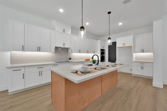 kitchen featuring sink, white cabinetry, decorative backsplash, hanging light fixtures, and a kitchen island with sink