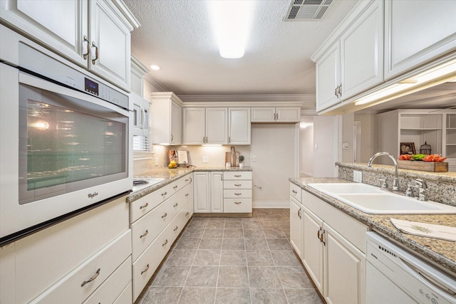 kitchen with light stone countertops, white appliances, white cabinets, and sink