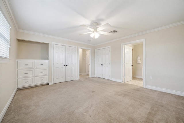 unfurnished bedroom featuring ensuite bath, light carpet, ceiling fan, crown molding, and multiple closets