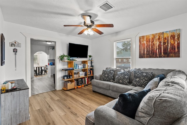 living room featuring ceiling fan, light wood-type flooring, and a textured ceiling