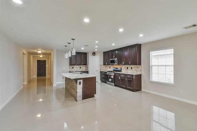 kitchen featuring stainless steel appliances, sink, decorative light fixtures, backsplash, and a kitchen island with sink