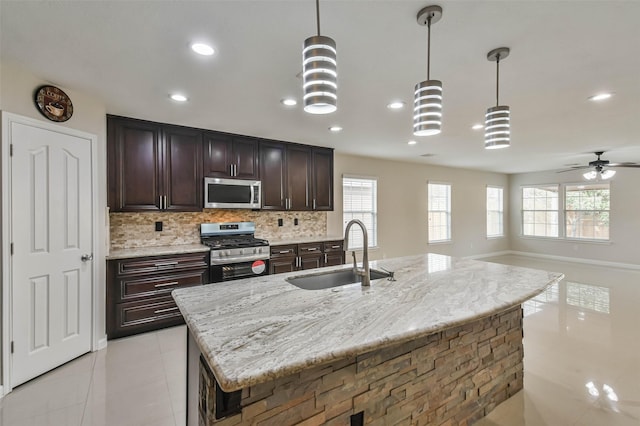 kitchen featuring sink, decorative backsplash, hanging light fixtures, light stone countertops, and appliances with stainless steel finishes