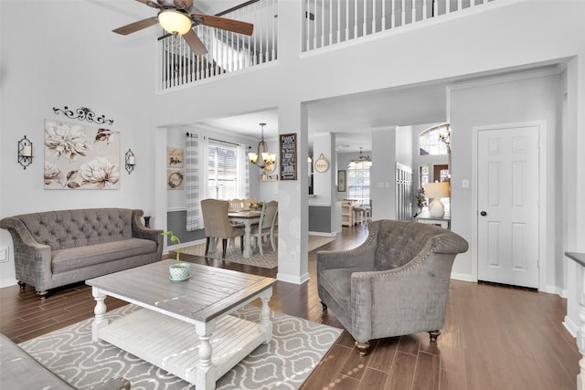 living room with a towering ceiling, dark hardwood / wood-style flooring, ceiling fan with notable chandelier, and crown molding