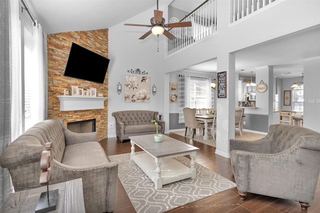 living room featuring a high ceiling, a fireplace, ceiling fan, and dark hardwood / wood-style flooring