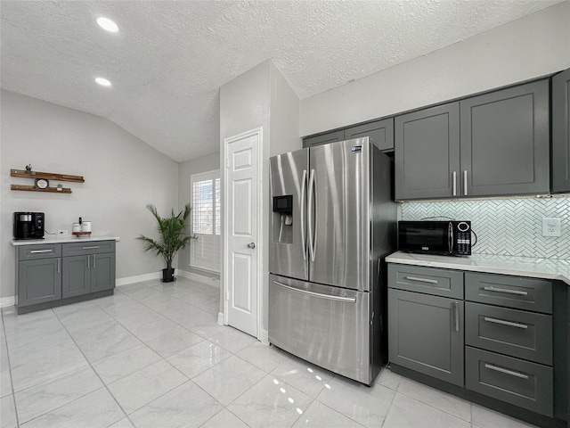 kitchen featuring vaulted ceiling, gray cabinetry, stainless steel refrigerator with ice dispenser, a textured ceiling, and backsplash