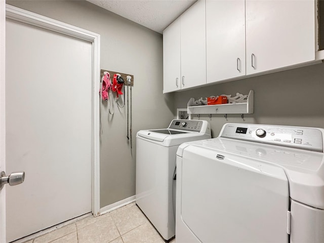 laundry area with a textured ceiling, cabinets, washing machine and clothes dryer, and light tile patterned floors