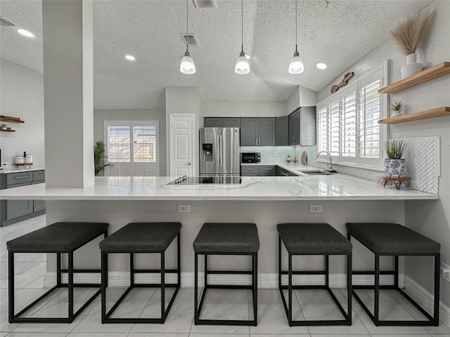 kitchen with gray cabinetry, kitchen peninsula, stainless steel fridge, a breakfast bar, and sink