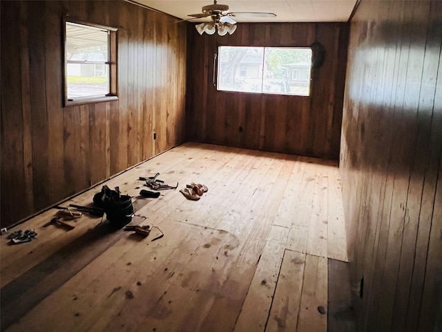 empty room with light wood-type flooring, ceiling fan, wooden walls, and a wealth of natural light