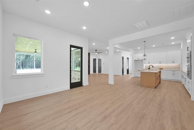 kitchen featuring hanging light fixtures, a center island with sink, light hardwood / wood-style floors, backsplash, and white cabinets