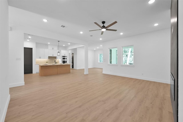 unfurnished living room with sink, light wood-type flooring, and ceiling fan