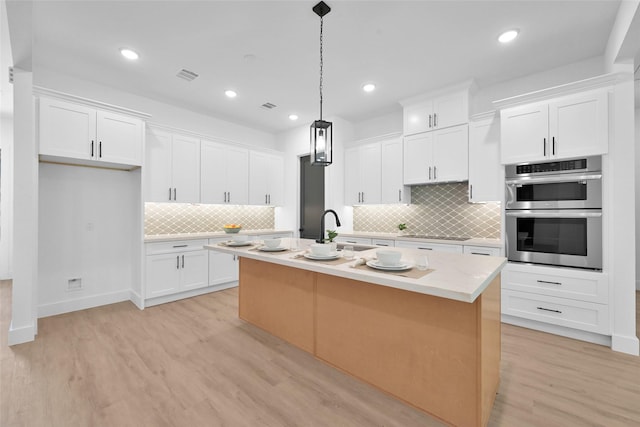 kitchen with stainless steel double oven, an island with sink, and white cabinetry