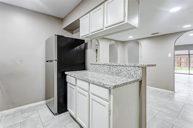 kitchen with white cabinetry, stainless steel refrigerator, light tile patterned floors, and light stone counters