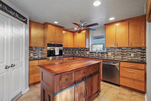 kitchen with a center island, butcher block counters, decorative backsplash, appliances with stainless steel finishes, and ceiling fan