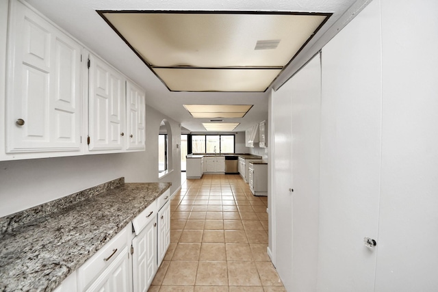 kitchen with light stone counters, white cabinets, dishwasher, and light tile patterned floors