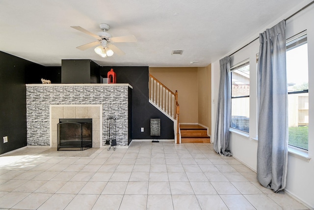 unfurnished living room featuring light tile patterned floors, a tile fireplace, ceiling fan, and a wealth of natural light