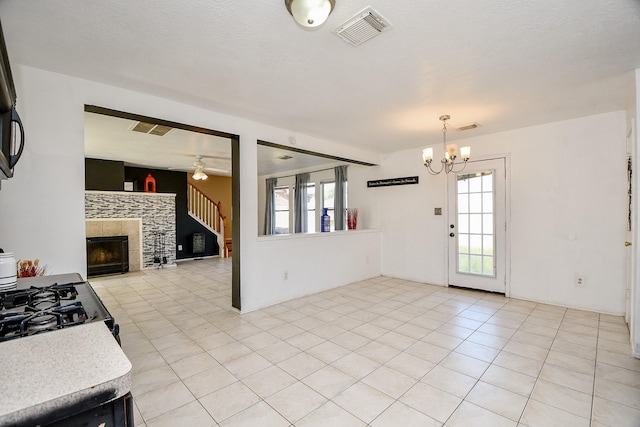 kitchen featuring gas stove, a tiled fireplace, ceiling fan with notable chandelier, and light tile patterned floors