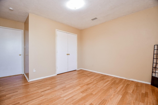 unfurnished bedroom with light wood-type flooring, a closet, and a textured ceiling