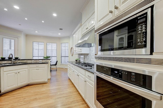 kitchen featuring sink, stainless steel appliances, white cabinetry, light hardwood / wood-style floors, and decorative backsplash