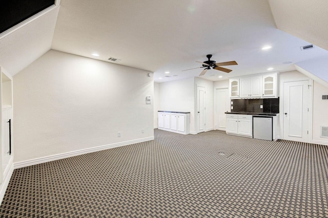 unfurnished living room with ceiling fan, vaulted ceiling, and dark colored carpet