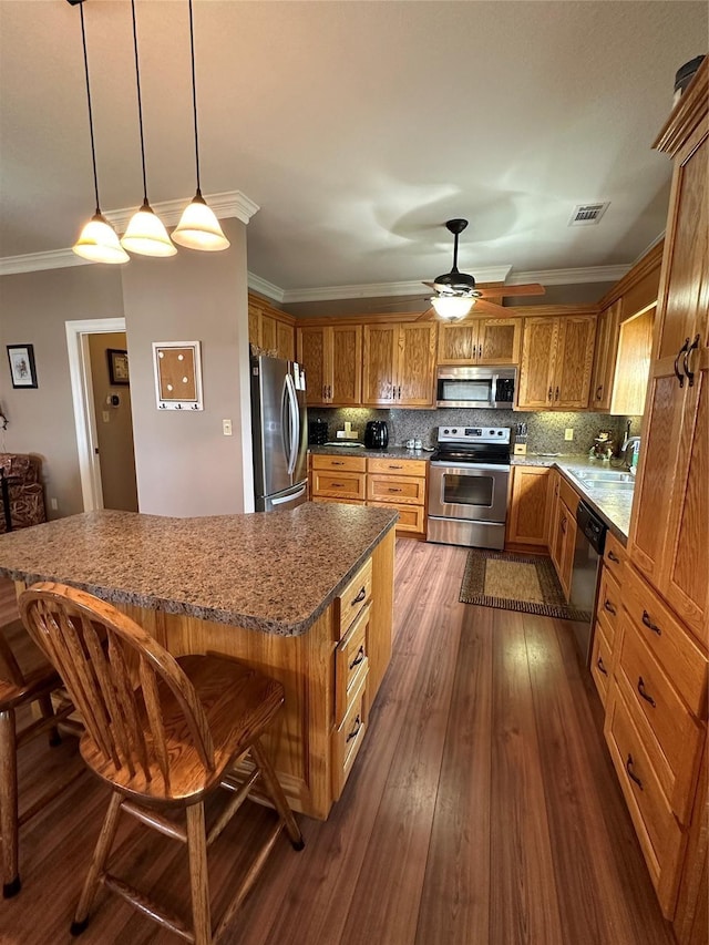 kitchen featuring a kitchen bar, ornamental molding, backsplash, pendant lighting, and appliances with stainless steel finishes