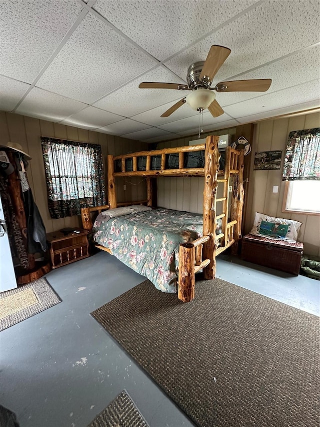 unfurnished bedroom featuring ceiling fan, multiple windows, concrete flooring, and a drop ceiling