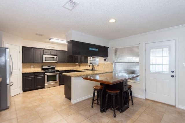 kitchen featuring kitchen peninsula, a breakfast bar area, appliances with stainless steel finishes, ornamental molding, and sink