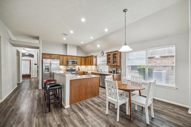 kitchen featuring decorative light fixtures, decorative backsplash, a kitchen island, dark hardwood / wood-style flooring, and appliances with stainless steel finishes