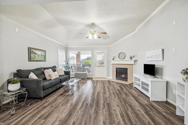 living room with dark wood-type flooring, a textured ceiling, vaulted ceiling, a tile fireplace, and ceiling fan