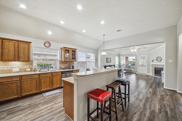 kitchen with vaulted ceiling, hanging light fixtures, a tile fireplace, a breakfast bar area, and ceiling fan