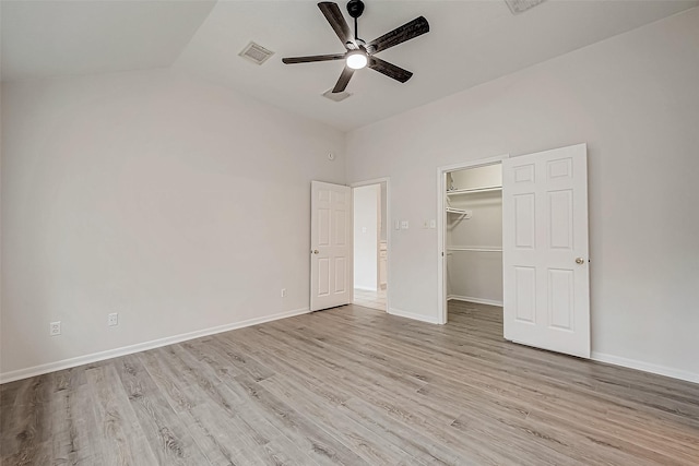 unfurnished bedroom with vaulted ceiling, ceiling fan, light wood-type flooring, a closet, and a walk in closet