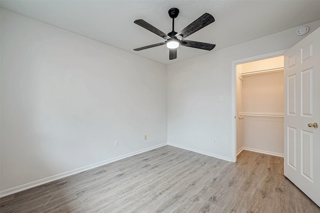 unfurnished bedroom with a closet, ceiling fan, light hardwood / wood-style flooring, and a spacious closet