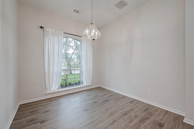 empty room featuring wood-type flooring, an inviting chandelier, and plenty of natural light