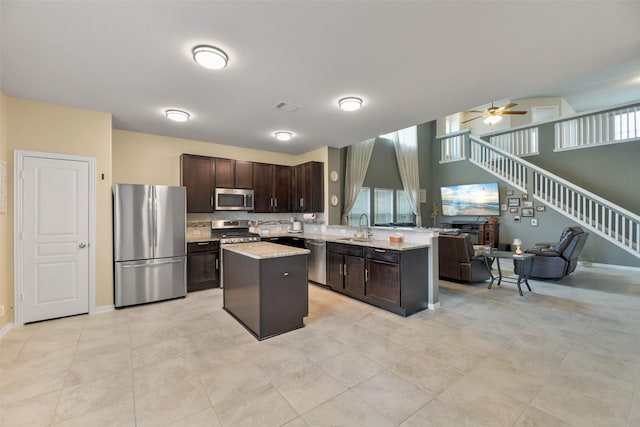 kitchen with stainless steel appliances, ceiling fan, a kitchen island, sink, and dark brown cabinets