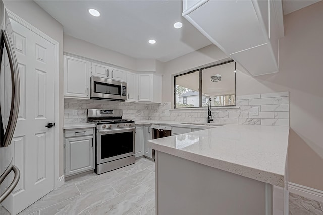 kitchen with light stone counters, kitchen peninsula, stainless steel appliances, white cabinetry, and sink