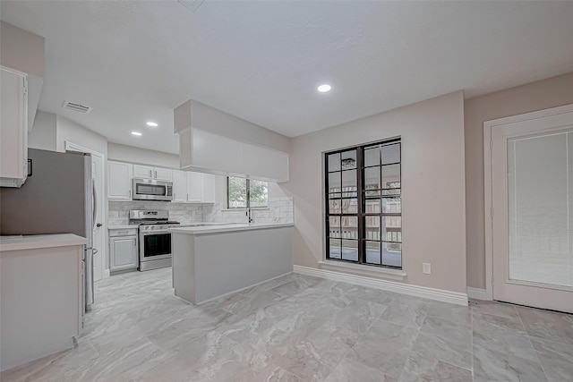 kitchen featuring kitchen peninsula, stainless steel appliances, white cabinets, and tasteful backsplash