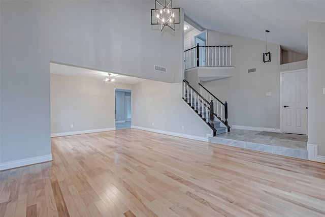 unfurnished living room with high vaulted ceiling, light hardwood / wood-style floors, and an inviting chandelier