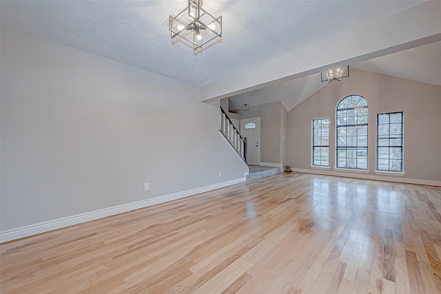 unfurnished living room featuring light hardwood / wood-style floors, lofted ceiling, a chandelier, and a textured ceiling